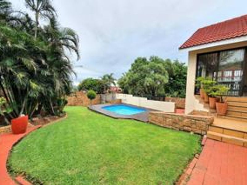 Rear garden area featuring a swimming pool, stone retaining wall, and a tiled patio leading to the main dwelling via sliding glass doors.