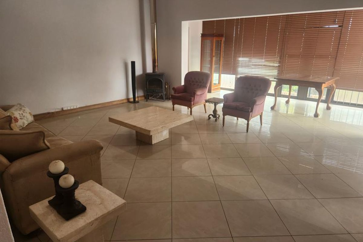 Spacious living area featuring large format floor tiles, a freestanding fireplace, and expansive windows with wooden blinds providing natural light.
