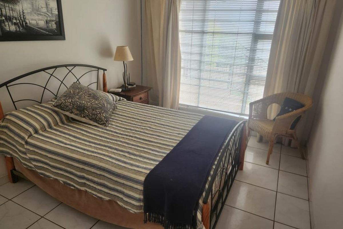 A functional bedroom featuring tiled flooring and large windows with venetian blinds, providing natural light and a neutral foundation for interior updates.
