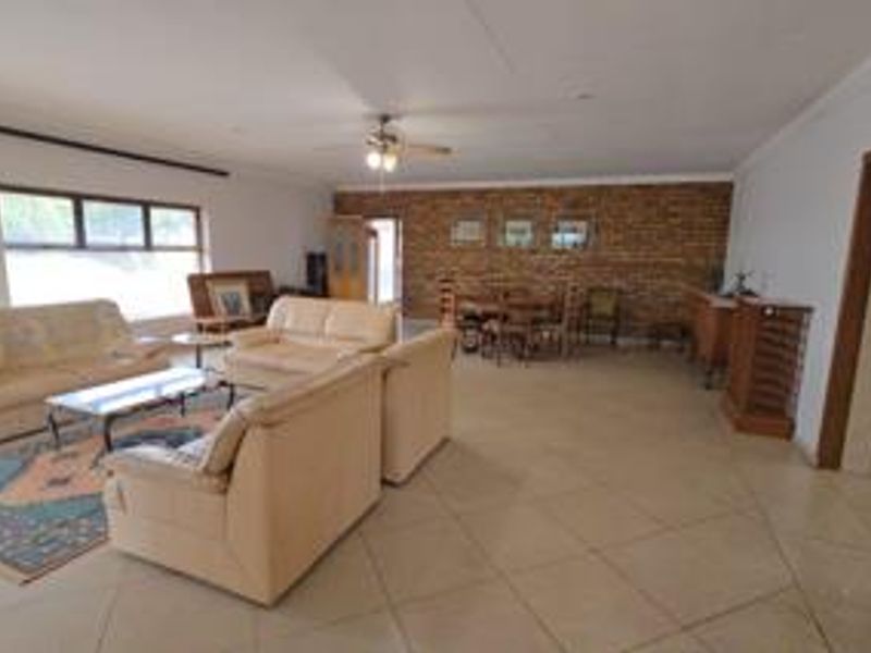 Spacious open-plan living and dining area featuring tiled flooring, an exposed brick feature wall, and a ceiling fan.