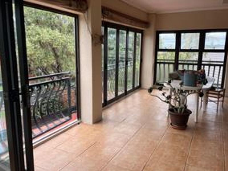 A spacious covered patio featuring tiled flooring, black aluminium folding doors, and a wrought iron balustrade with views of the surrounding garden.