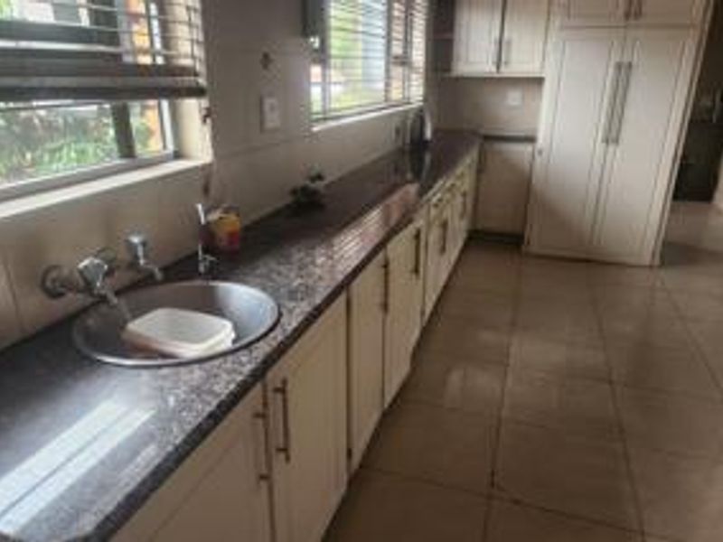 A functional kitchen featuring ample built-in cabinetry, granite countertops, a stainless steel sink, and tiled flooring with natural light from the window.