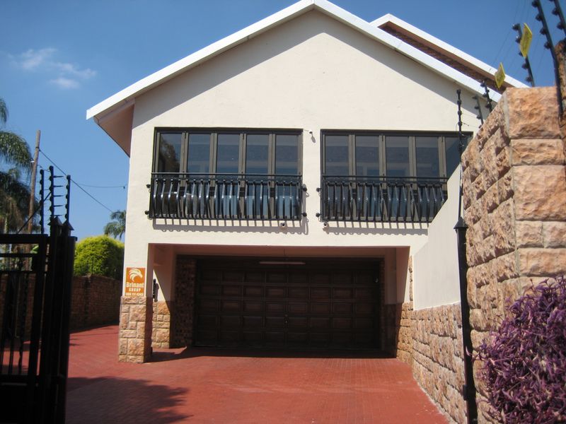 Front elevation of a duet property featuring a double garage, paved driveway, and an upper level with folding doors and a balcony.