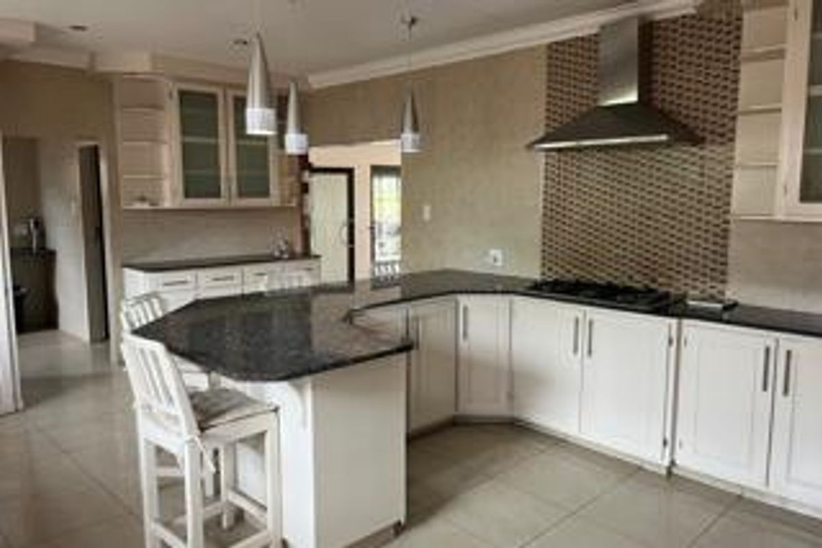A well-appointed kitchen featuring granite countertops, white cabinetry, a gas hob with a stainless steel extractor fan, and tiled flooring.