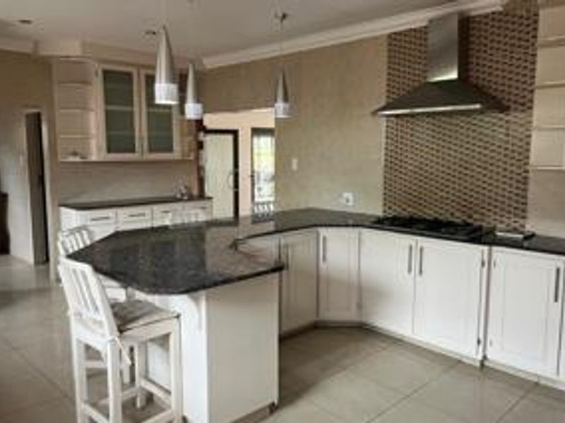 A well-appointed kitchen featuring granite countertops, white cabinetry, a gas hob with a stainless steel extractor fan, and tiled flooring.