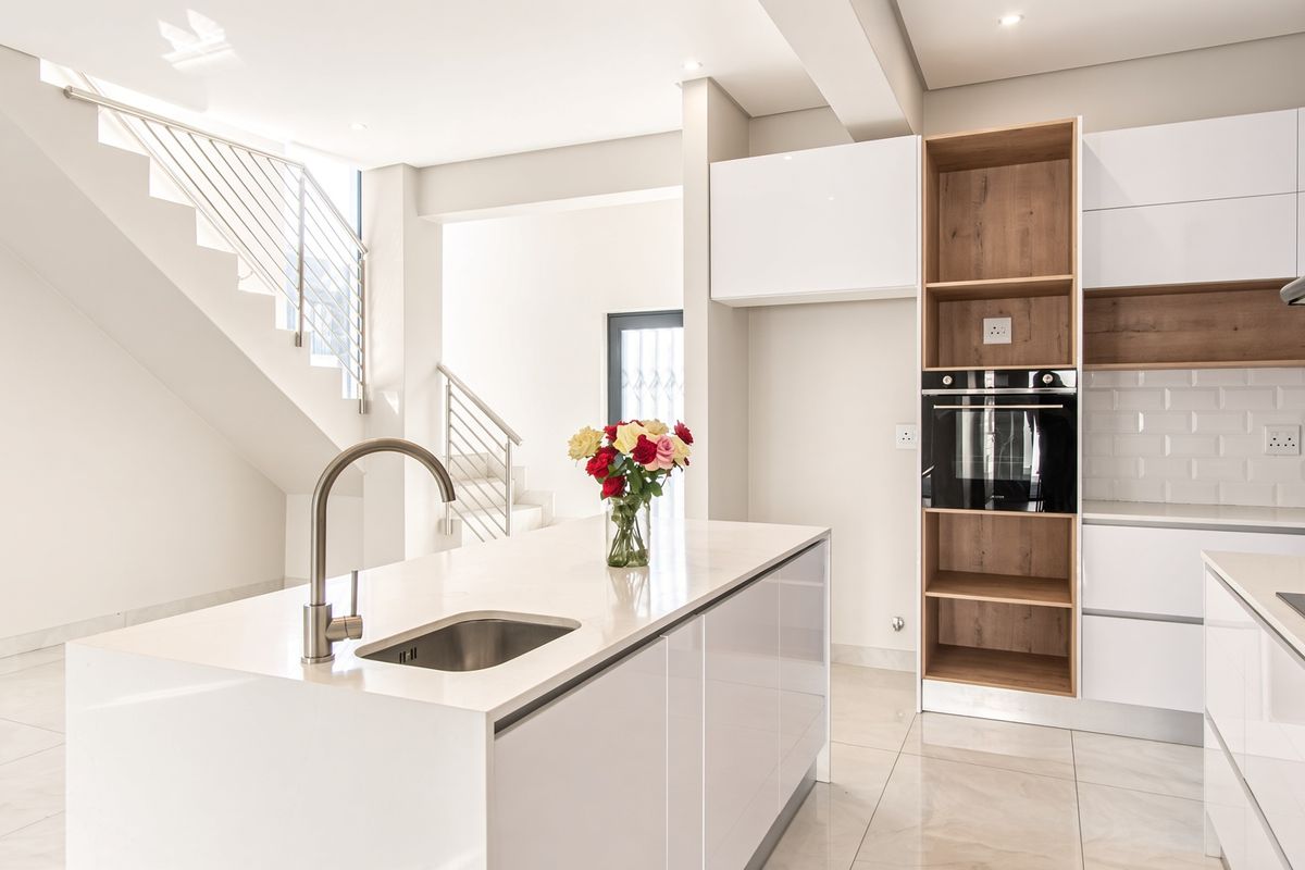 Modern kitchen featuring a central island, built-in oven, gas hob, subway tile backsplash, and sleek white cabinetry, adjacent to an open staircase.