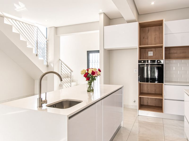 Modern kitchen featuring a central island, built-in oven, gas hob, subway tile backsplash, and sleek white cabinetry, adjacent to an open staircase.