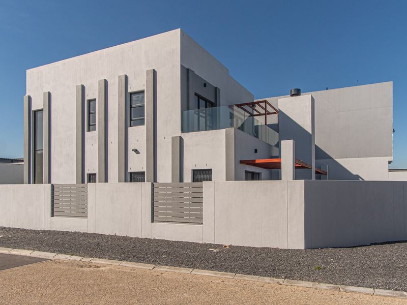 Modern two-story residential property featuring a clean rendered facade, glass balcony balustrade, timber pergola, and secure boundary wall with integrated metal fencing.