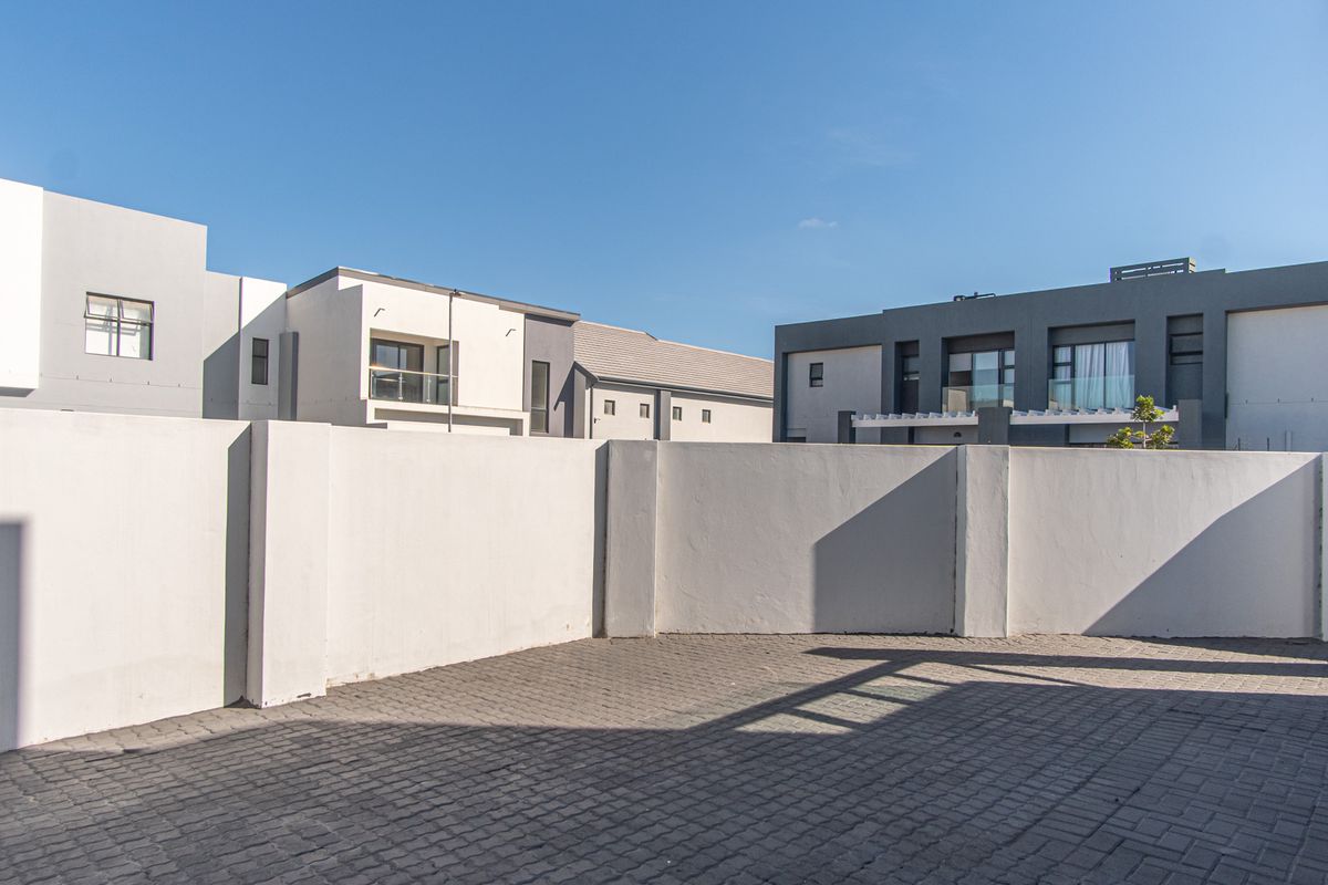 A paved rear courtyard area enclosed by a high boundary wall, situated within a modern residential complex.