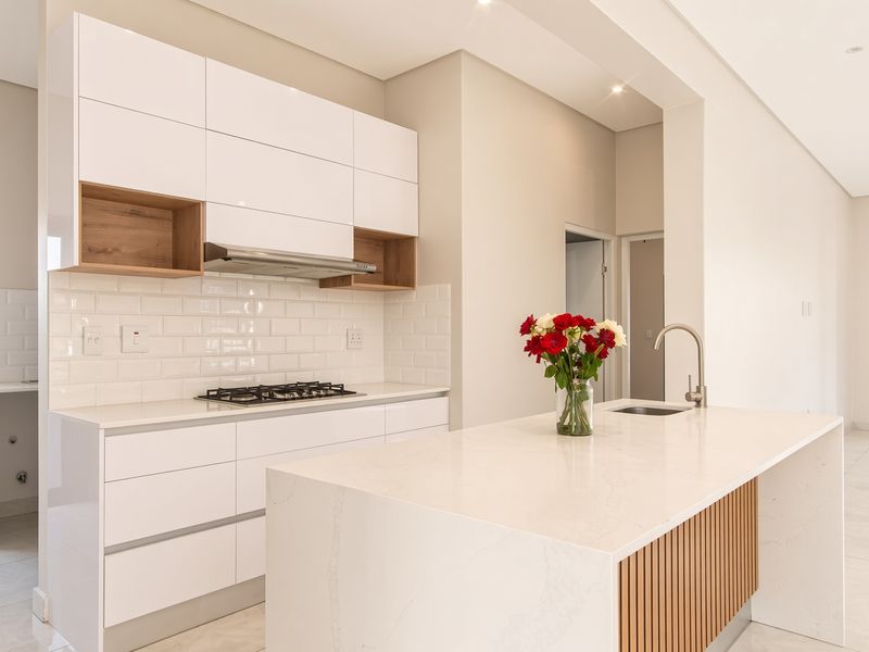 Modern kitchen featuring white cabinetry, stone countertops, a central island with sink, gas cooktop, and subway tile backsplash in a bright, open-plan space.