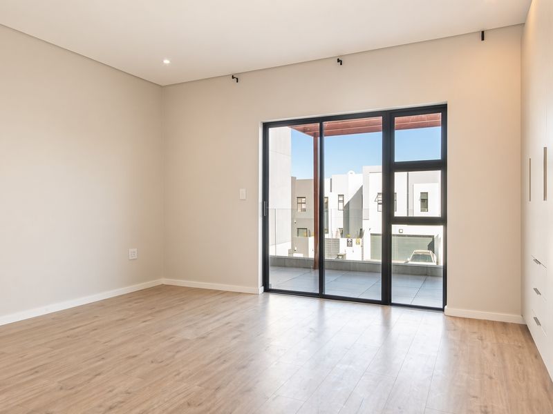 A bright, modern bedroom featuring neutral walls, laminate flooring, built-in cupboards, and a large sliding glass door leading to an outdoor patio area.