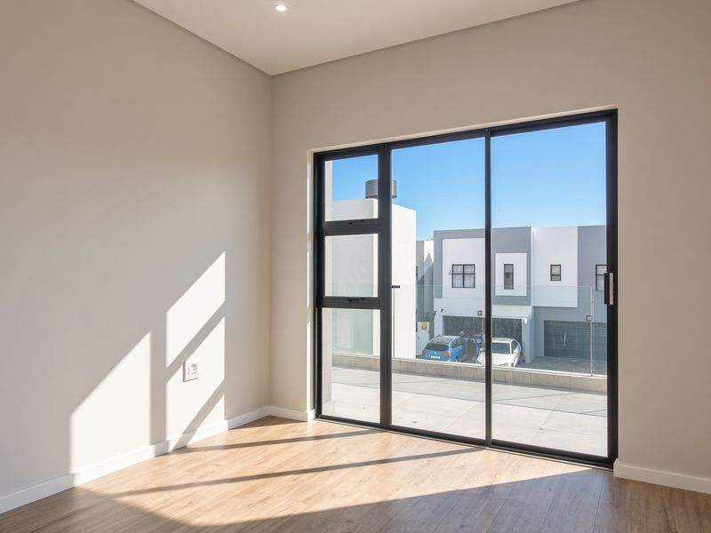A bright, empty bedroom featuring modern laminate flooring and a large black aluminium sliding door providing access to an outdoor area.