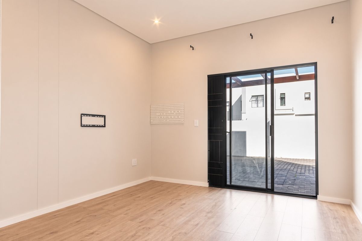 A bright, modern, and empty living room featuring light laminate flooring, neutral walls, and a large sliding glass door leading to an outdoor paved area.