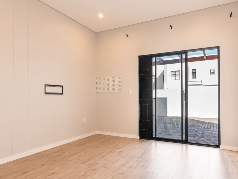 A bright, modern, and empty living room featuring light laminate flooring, neutral walls, and a large sliding glass door leading to an outdoor paved area.