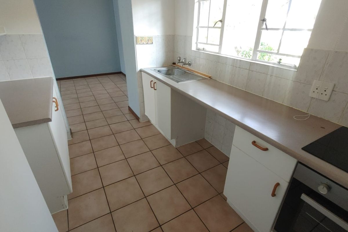 A functional, empty kitchen featuring built-in cabinetry, laminate countertops, a stainless steel sink, and an integrated oven with an electric hob.