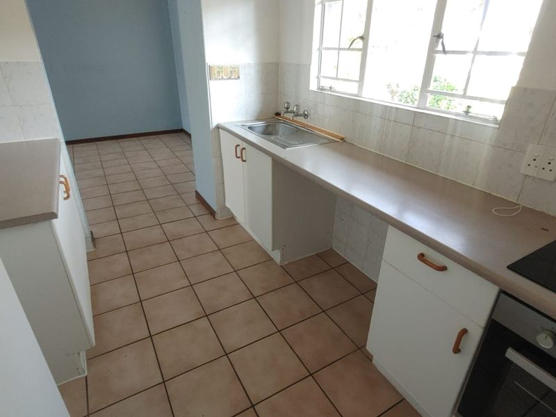 A functional, empty kitchen featuring built-in cabinetry, laminate countertops, a stainless steel sink, and an integrated oven with an electric hob.
