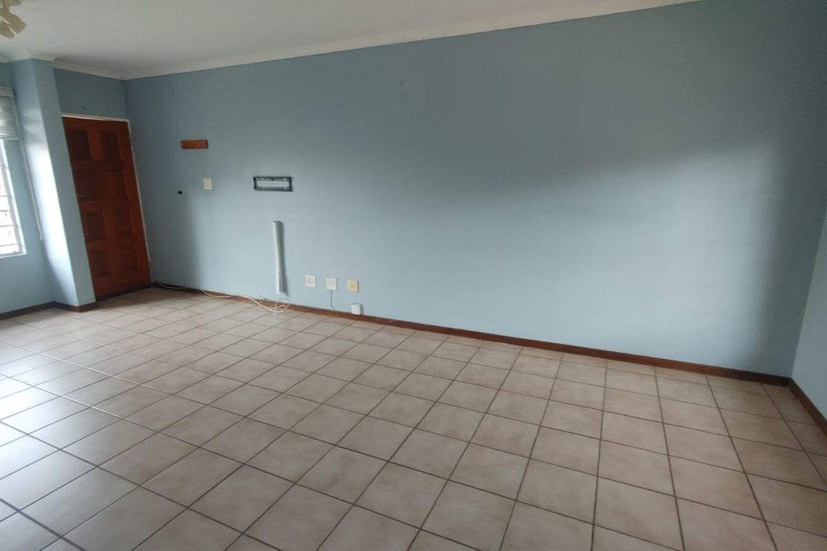 An empty living room featuring tiled flooring, blue painted walls, and natural light from windows with security bars.