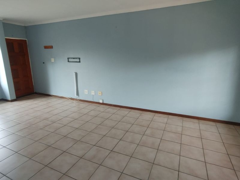 An empty living room featuring tiled flooring, blue painted walls, and natural light from windows with security bars.