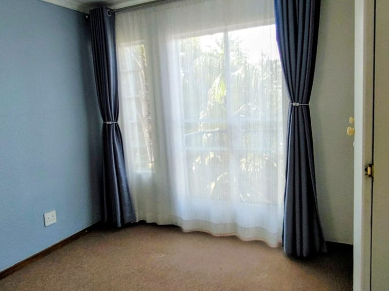 A bright, empty bedroom featuring carpeted flooring and a large sliding glass door that provides natural light and access to the outdoors.