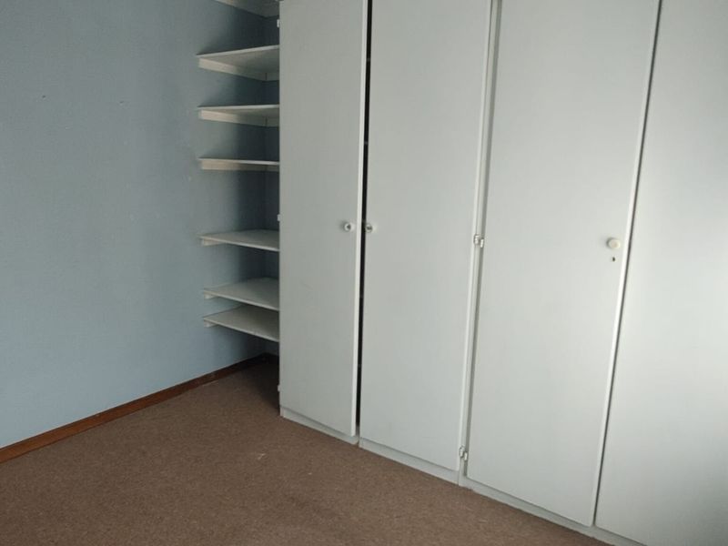 A vacant bedroom featuring built-in cupboards with integrated open shelving and carpeted flooring, ready for a modern update.
