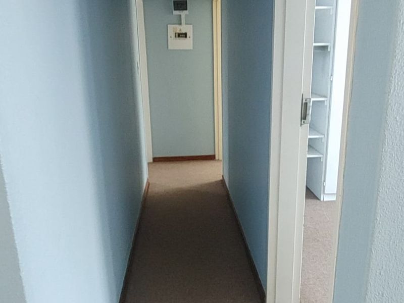 A functional apartment hallway featuring carpeted flooring, a ceiling light, and access to adjacent rooms with built-in shelving visible.