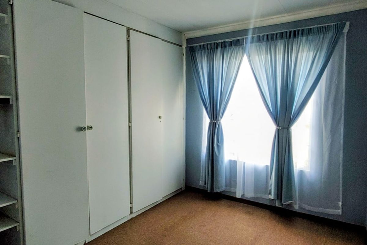 A clean, empty bedroom featuring built-in cupboards and carpeted flooring, offering a neutral space ready for personalization.