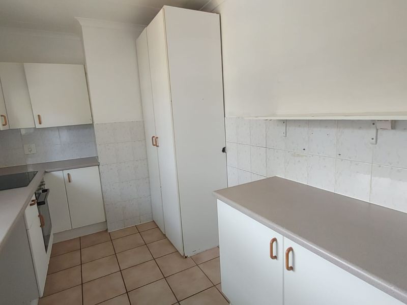 A functional kitchen featuring white built-in cabinetry, laminate countertops, ceramic tile backsplash, and tiled flooring, offering a clean and practical workspace.