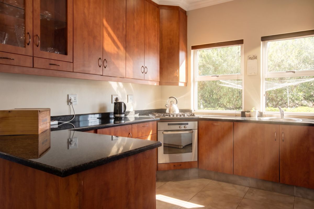 A functional kitchen featuring warm-toned wooden cabinetry, dark granite countertops, a built-in oven, gas hob, and natural light from dual windows.