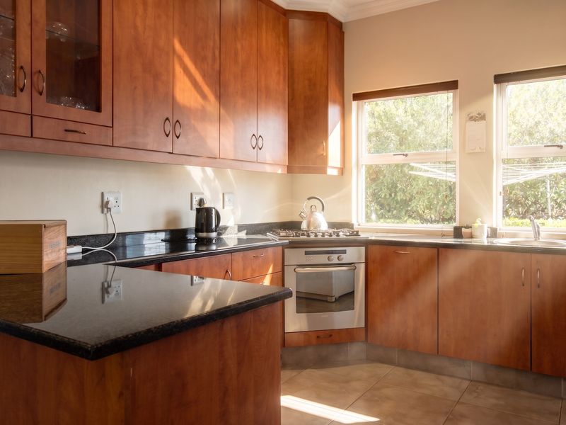 A functional kitchen featuring warm-toned wooden cabinetry, dark granite countertops, a built-in oven, gas hob, and natural light from dual windows.