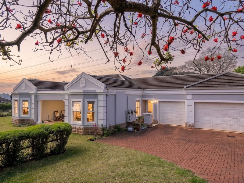 Front elevation of a well-maintained townhouse featuring a double garage, brick paved driveway, stone cladding accents, and a covered patio area.