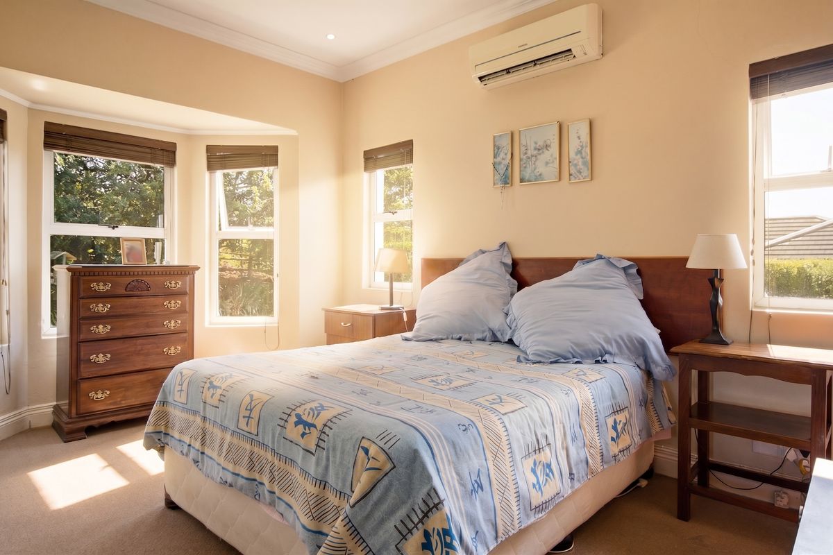 A well-lit bedroom featuring a bay window, neutral wall tones, carpeted flooring, and a wall-mounted split-system air conditioning unit.