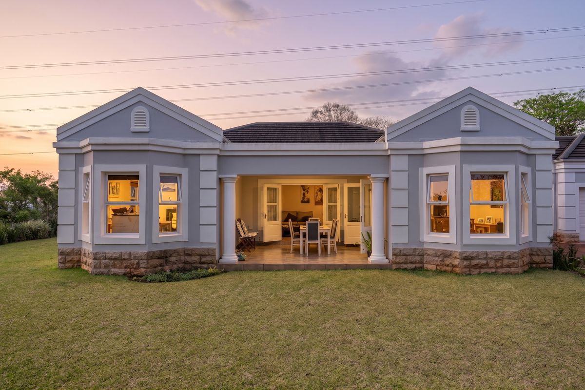 Rear view of a well-maintained townhouse featuring a covered patio, stone-clad base, and symmetrical architectural design overlooking a private garden.
