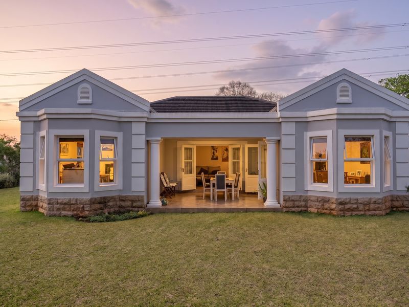 Rear view of a well-maintained townhouse featuring a covered patio, stone-clad base, and symmetrical architectural design overlooking a private garden.
