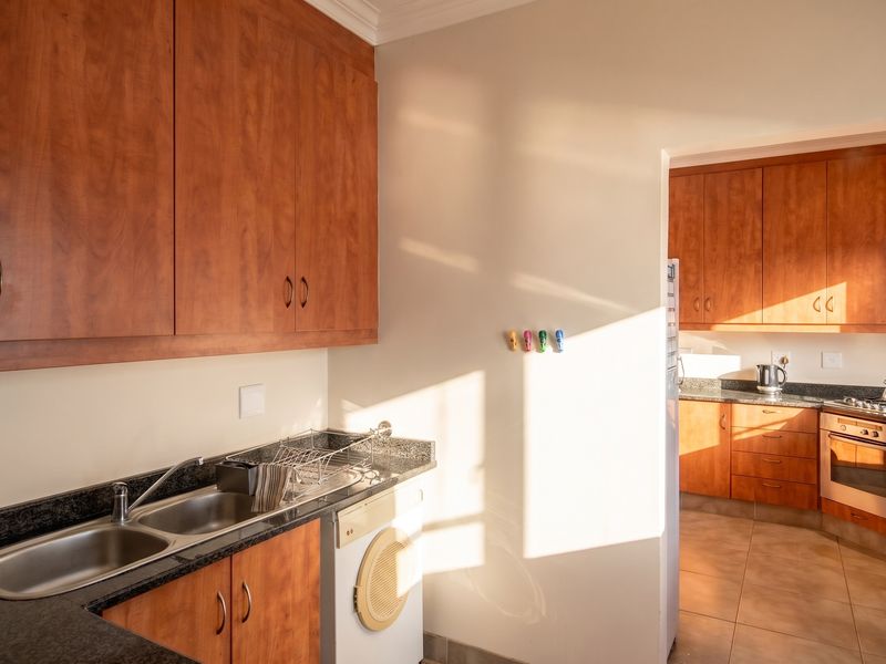 A functional scullery area featuring granite countertops, double sink, and ample wooden cabinetry, with an adjacent view into the main kitchen area.