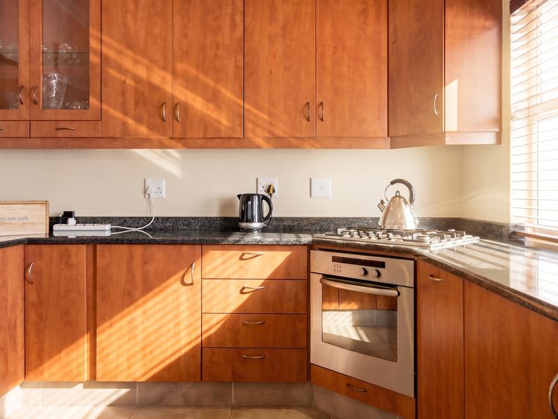 A functional kitchen featuring warm-toned wooden cabinetry, granite countertops, and integrated stainless steel oven and gas hob, illuminated by natural light.