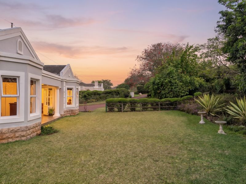 A well-maintained rear exterior view of the townhouse featuring stone cladding, a covered patio area, and a spacious landscaped garden at sunset.