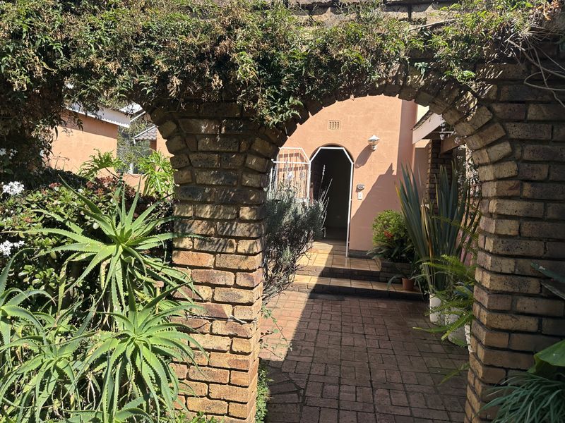 A charming brick-arched entrance pathway leading to the front door, featuring paved flooring and established garden landscaping.