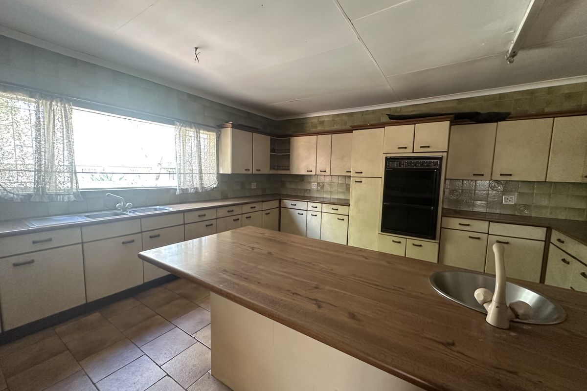Spacious kitchen featuring extensive built-in cabinetry, a central island with a secondary sink, and a double wall oven, offering significant potential for modernization.