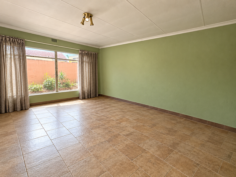 A spacious, empty living room featuring neutral ceramic tile flooring, large windows, and green painted walls, offering a blank canvas for interior design.
