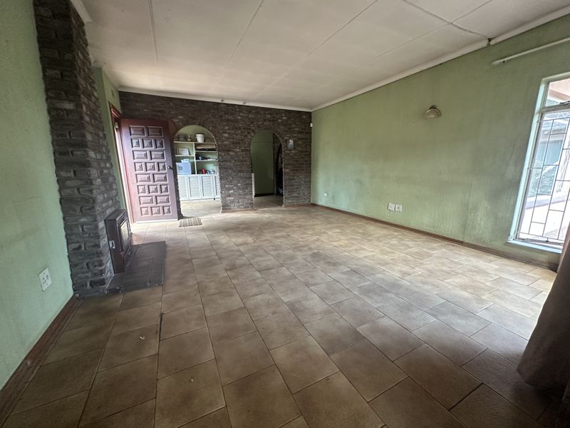 Spacious living room featuring a brick fireplace, tiled flooring, and arched entryways, offering a blank canvas for renovation and interior design.