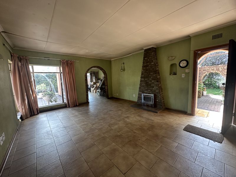 Spacious living room featuring a brick fireplace with a wood-burning stove, tiled flooring, and an arched entryway leading to adjacent living spaces.