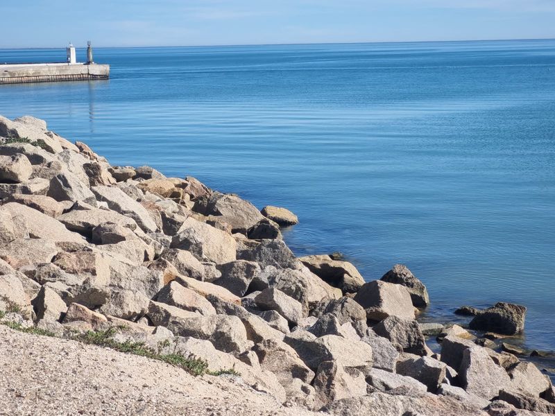 A scenic view of the coastline featuring a rocky shoreline and a distant breakwater with a navigation beacon.