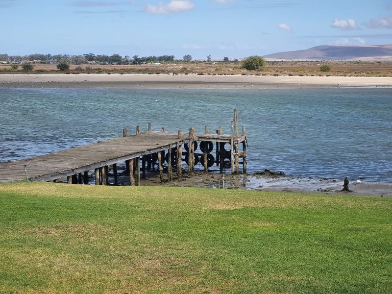 A scenic view of a waterfront property featuring a grass lawn leading to a weathered wooden jetty extending into the water.