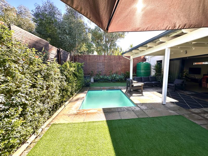 A private outdoor pool area featuring a covered patio, artificial lawn, and timber privacy fencing, creating a low-maintenance entertainment space.