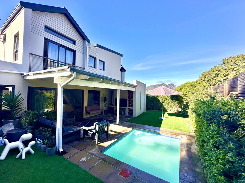 Rear exterior view of the townhouse featuring a covered patio, built-in fireplace, swimming pool, and a well-maintained garden area.