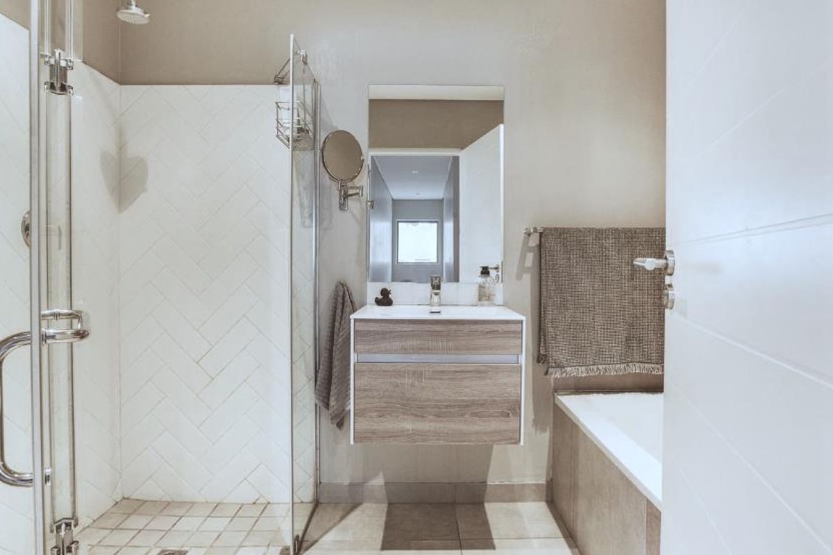 Modern bathroom featuring a walk-in shower with herringbone tiling, a wall-mounted vanity, and a bathtub, finished with contemporary fixtures.