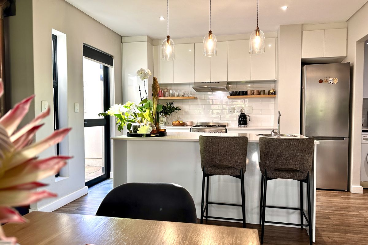 Modern kitchen featuring white cabinetry, subway tile backsplash, stone countertops, integrated gas hob, and a breakfast bar with pendant lighting.