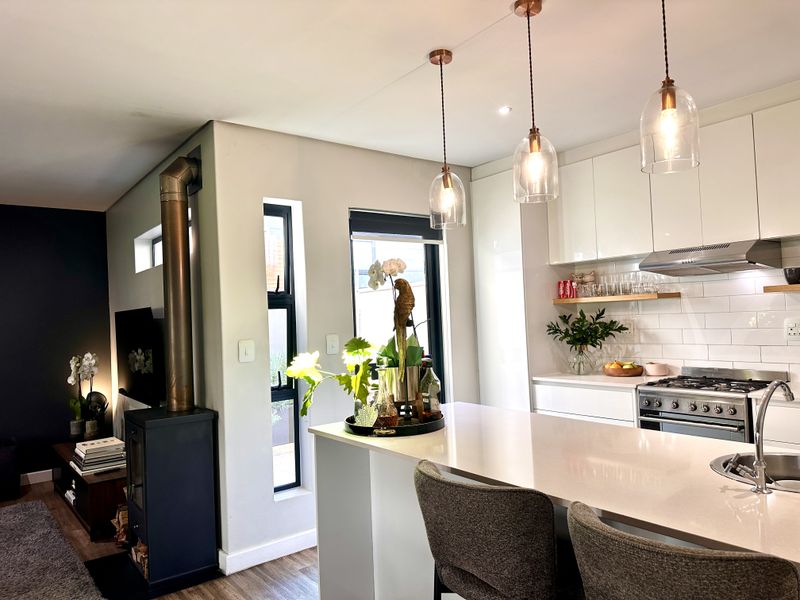 Modern open-plan kitchen and living area featuring a sleek kitchen island, gas stove, subway tile backsplash, and a contemporary freestanding fireplace.