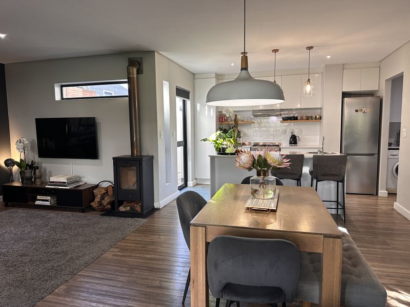 Modern open-plan living area featuring a wood-burning fireplace, dining space, and a contemporary kitchen with subway tile backsplash and integrated cabinetry.