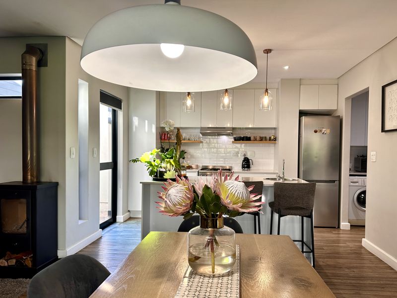 Modern open-plan living and kitchen area featuring a wood-burning fireplace, sleek cabinetry, subway tile backsplash, and a functional kitchen island with breakfast bar seating.